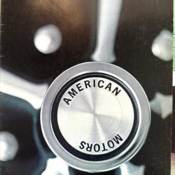 Close-up of a chrome circular emblem with the words 'AMERICAN MOTORS' around the center, viewed from above, with '1969' in the top-left corner.