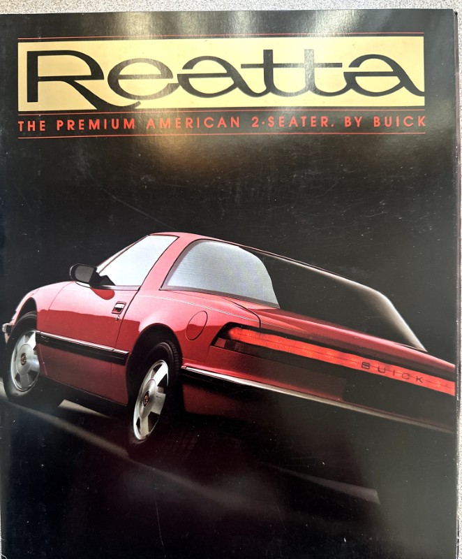IMG_5653 | Merrick Auto Museum Red Buick Reatta two-seater brochure cover with a rear-three-quarter view of the car against a black background and the title 'Reatta' above, plus the subtitle 'The Premium American 2-Seater, by Buick'.