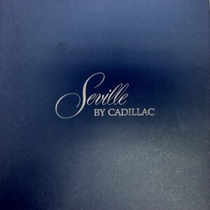 Cover of a Cadillac Seville booklet with white script text 'Seville by Cadillac' on a dark blue background, likely a brochure or manual cover.