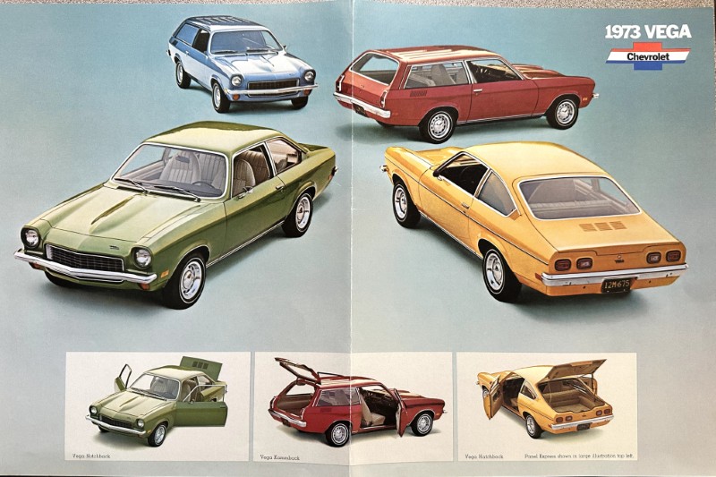 IMG_5938 | Merrick Auto Museum 1973 Vega Chevrolet lineup: four colored cars (green coupe, yellow hatchback, red wagon, blue wagon) on a blue backdrop with Chevrolet logo in corner.