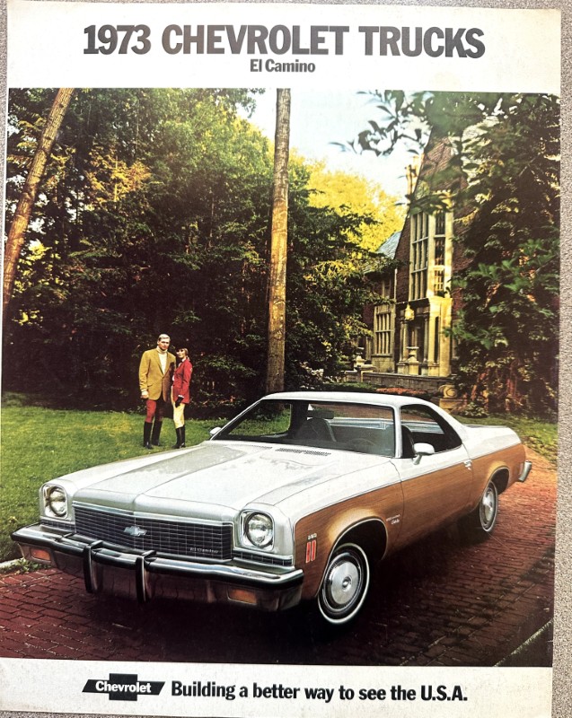 IMG_5947 | Merrick Auto Museum Advertisement image for a 1973 Chevrolet El Camino: a silver-and-trown car parked on a brick driveway with a mansion and trees in the background, and a couple standing nearby under a banner that reads '1973 CHEVROLET TRUCKS'.