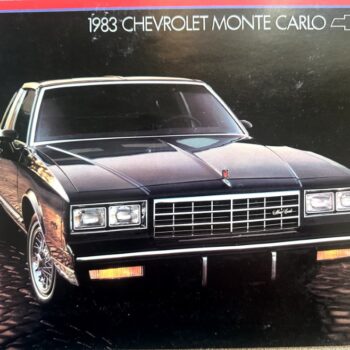 Front view of a black 1983 Chevrolet Monte Carlo with a chrome grille and rectangular headlights on a cobblestone surface.