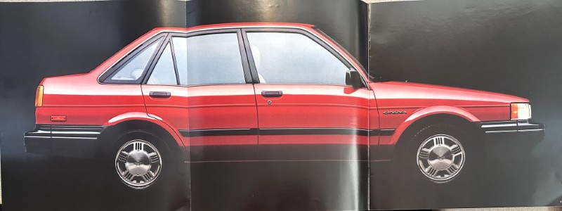 IMG_6123 | Merrick Auto Museum Side view of a red, four-door sedan with chrome trim and hubcaps against a dark background.