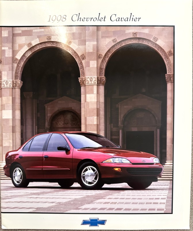 IMG_6180 | Merrick Auto Museum Red 1998 Chevrolet Cavalier parked in front of arched stone architecture with a Chevrolet logo below.