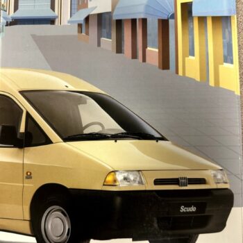 Yellow Fiat Scudo van in the foreground on a city street, with storefronts and blue awnings in the background; 'FIAT SCUDO' headline visible at top.
