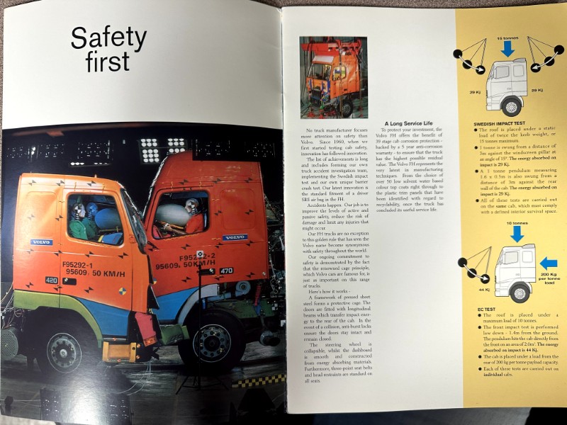 IMG_8695 | Merrick Auto Museum Two orange Volvo trucks being inspected in a workshop under a 'Safety first' header on the left page. Right page shows diagrams and text about safety tests.