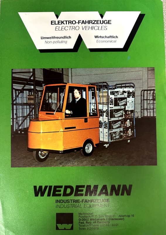 IMG_8738 | Merrick Auto Museum Green Wiedemann industrial equipment brochure featuring an orange electric forklift pulling a rack of boxed goods in a warehouse setting.