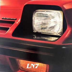 Close-up of a red car front showing a square headlight and black surround with a Mercury badge.