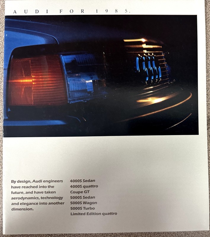IMG_9340 | Merrick Auto Museum Close-up of an Audi car's front end—grille, headlight, and bumper, from a 1985 brochure page with model list below.