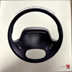 Black Saturn steering wheel with cruise control buttons on left and right, and S-Series logo bottom-right of the brochure page.