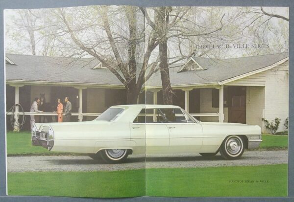 16 Custom | Merrick Auto Museum Vintage white Cadillac De Ville sedan parked on a gravel driveway in front of a ranch-style house, with people on the porch in the background.