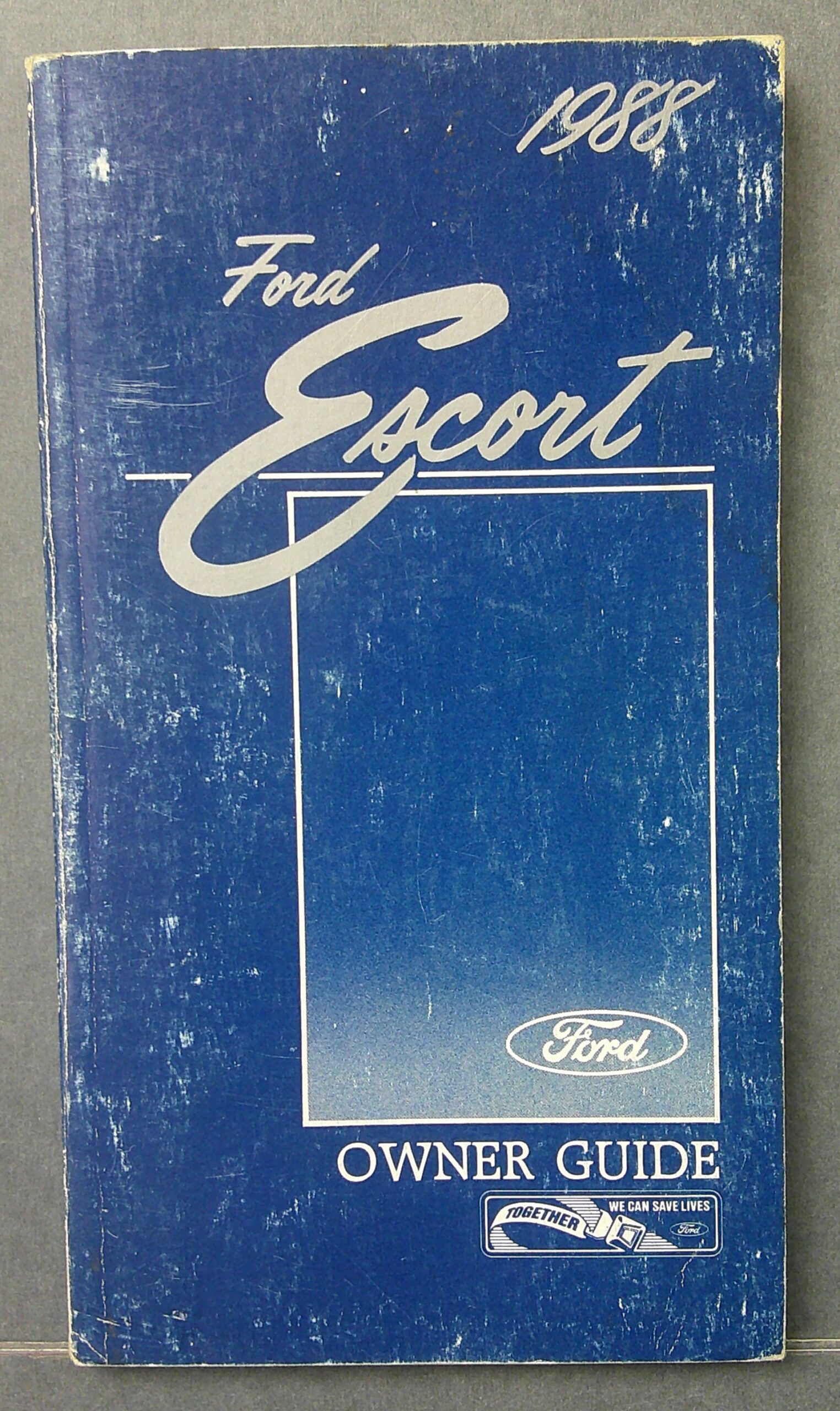 Digital Camera | Merrick Auto Museum Blue Ford Escort Owner’s Guide booklet with white logo and worn cover art, 1980s style typography.