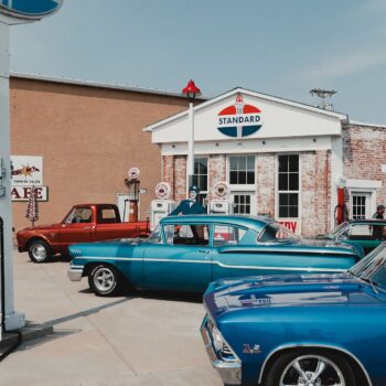 Retro gas station and car lot with bright blue 1950s-era cars lined up in front of a white brick building with a Standard sign above the entrance