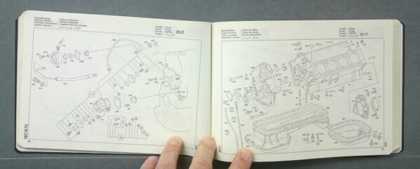 Blk2 Custom | Merrick Auto Museum Open repair manual with exploded diagrams of engine parts; a hand holds the bottom edge of the pages.