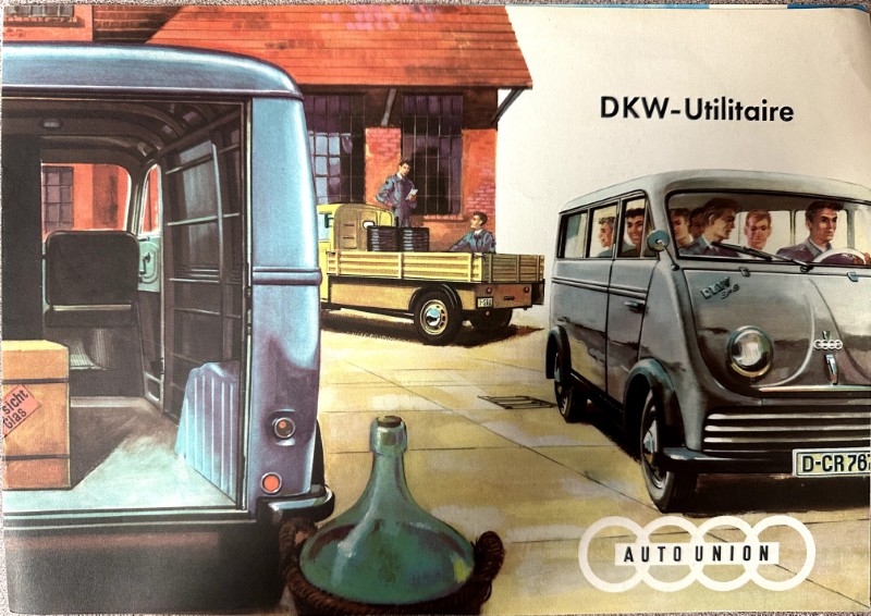IMG_9495 | Merrick Auto Museum Vintage illustration of a DKW-Utilitaire delivery van at a loading yard with workers loading crates from a pickup truck outside a brick building, Auto Union logo visible.
