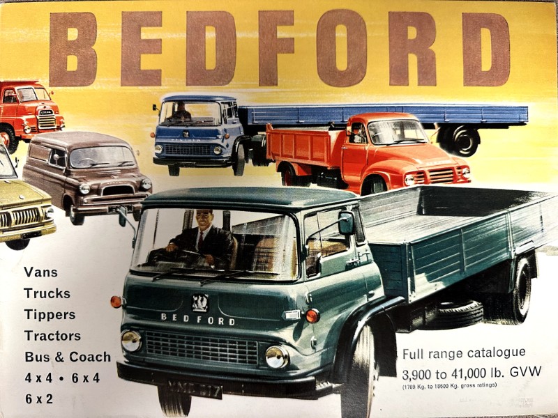 IMG_9582 | Merrick Auto Museum Vintage Bedford truck advertisement showing a green flatbed Bedford truck in the foreground with a yellow backdrop and multiple other Bedford trucks in the background; text lists vans, trucks, tippers, tractors, buses & coaches and notes a full-range catalogue with GVW figures.